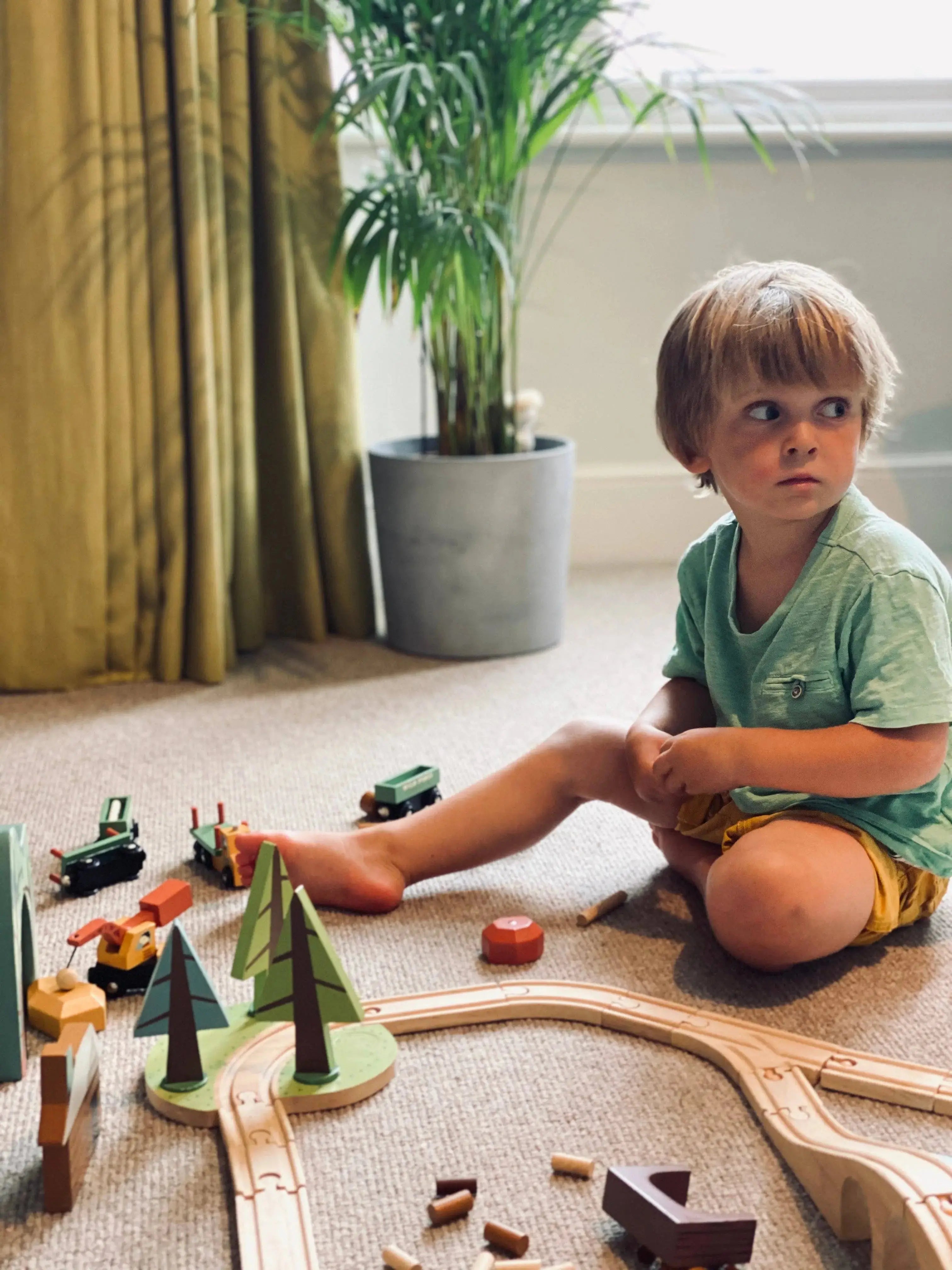 Kind beim fantasievollen Spielen mit Holzeisenbahn, Schienen und Landschaftselementen