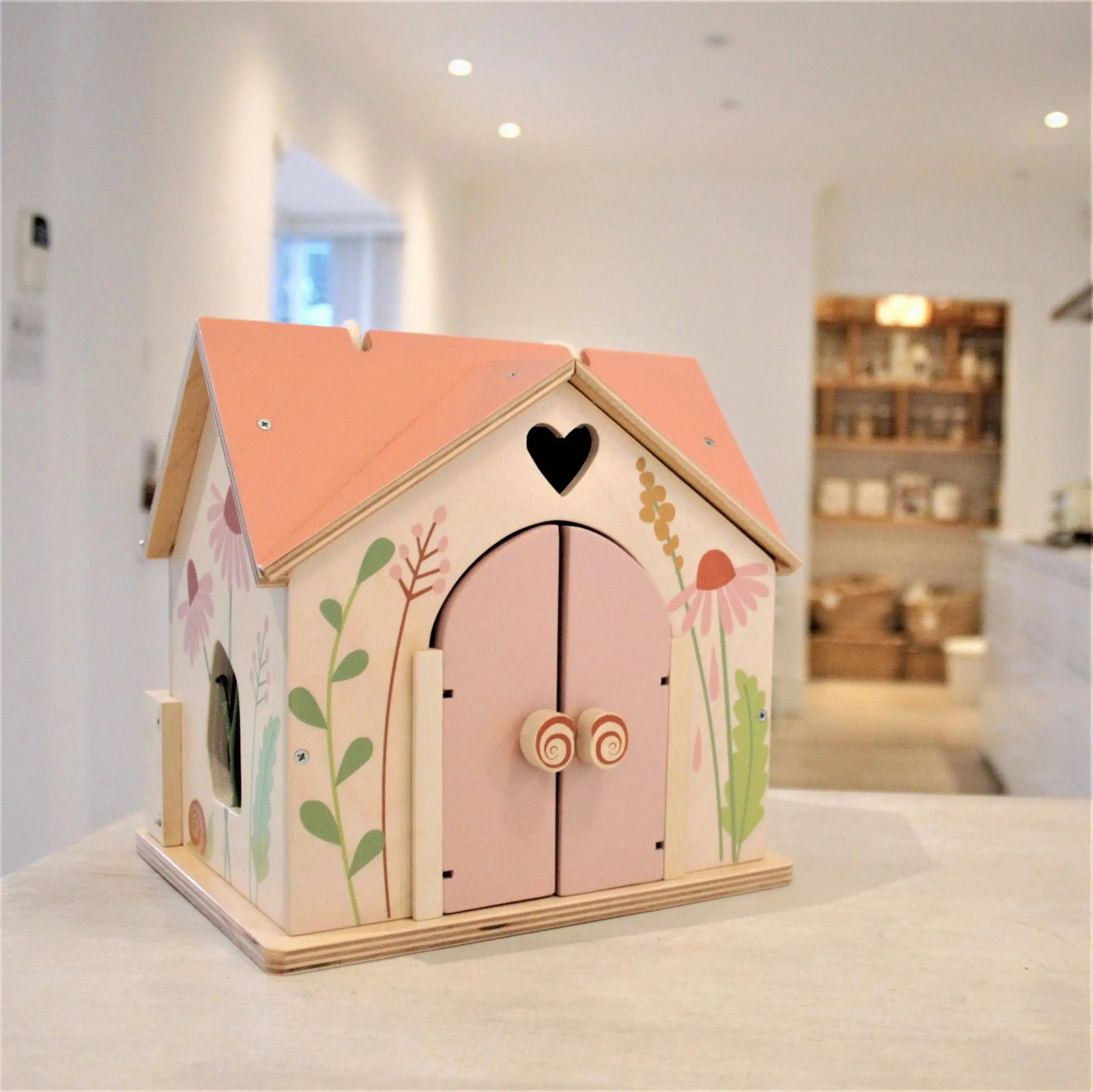 Holzpuppenhaus mit rosa Dach und Garten als Spielzeug im Kinderzimmer