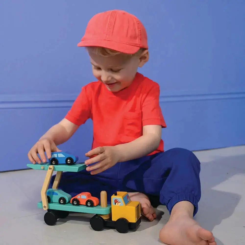 Kind beim fantasievollen Rollenspiel mit dem Autotransporter und den farbigen Holzautos.