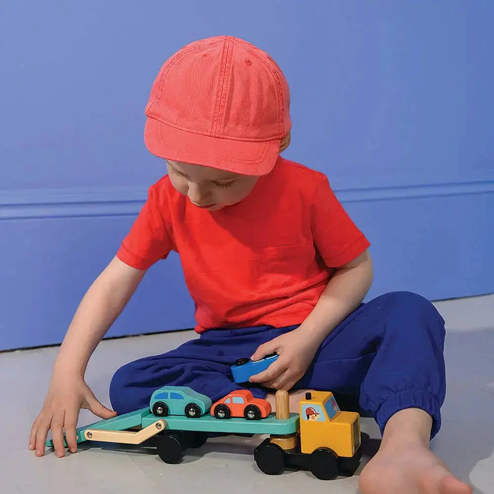 Kind bewegt den beladenen Autotransporter über den Boden und spielt mit den Fahrzeugen.