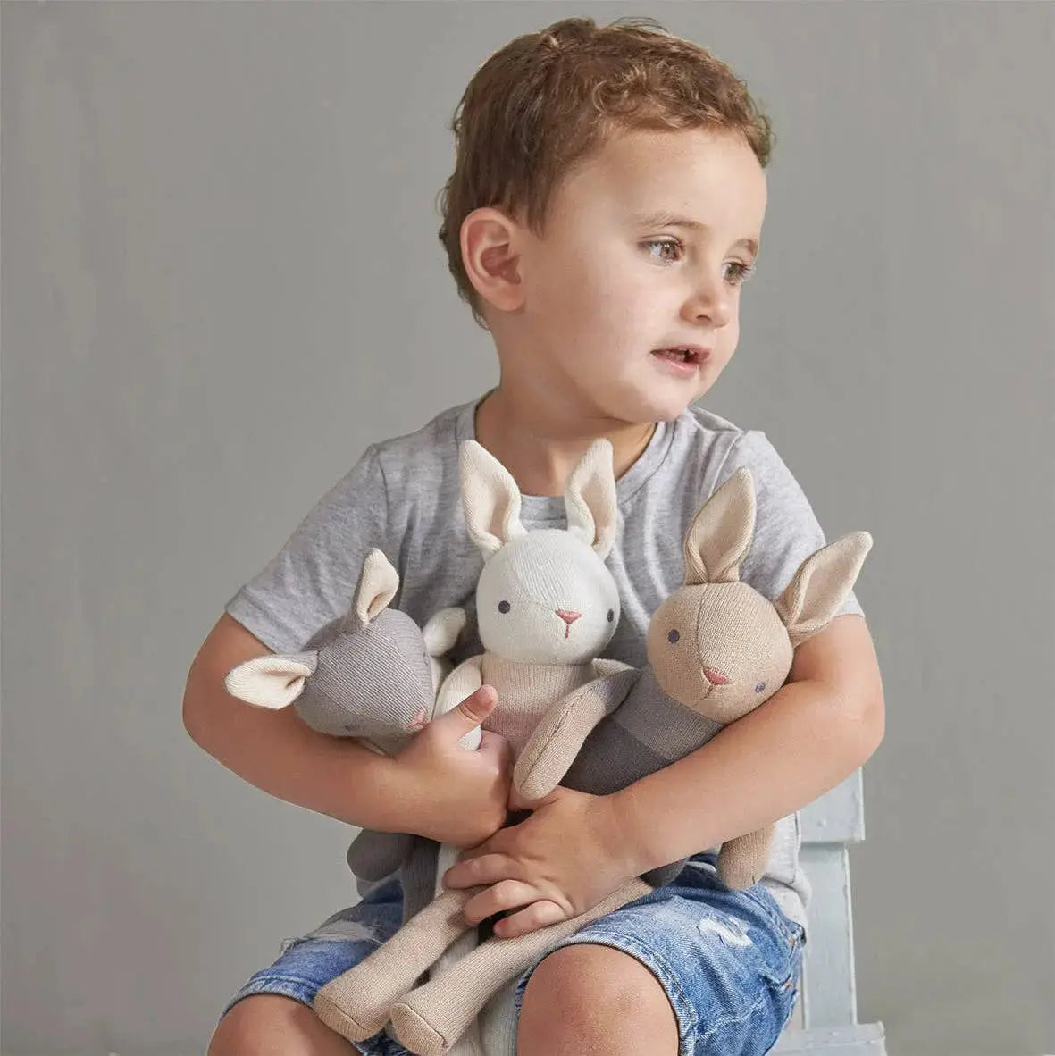 Kind hält die gestrickte Hasenpuppe in Creme als weichen Kuschelfreund im Arm.