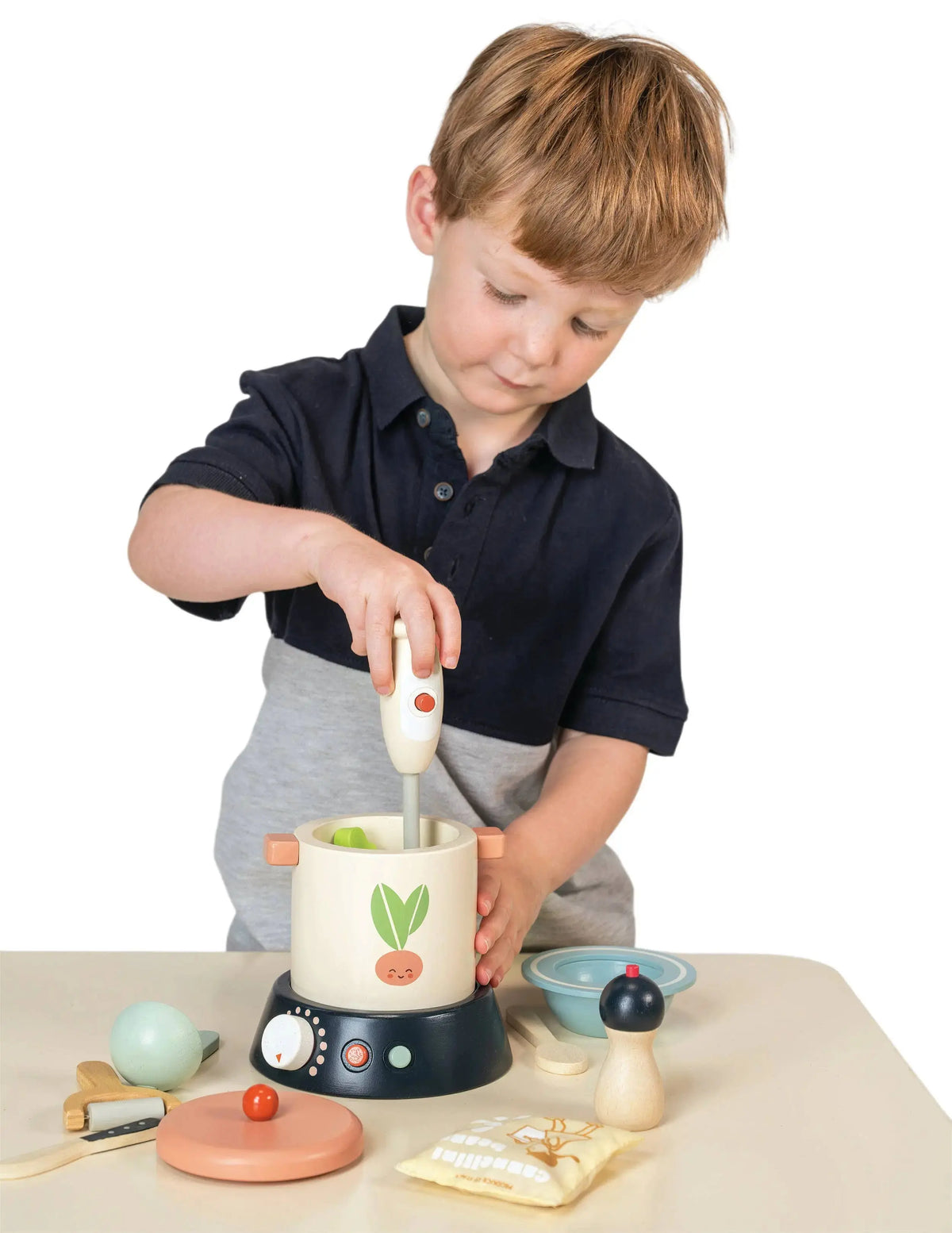 Kind bereitet beim Rollenspiel eine Suppe mit Kochtopf, Handmixer und Gemüse aus Holz zu.
