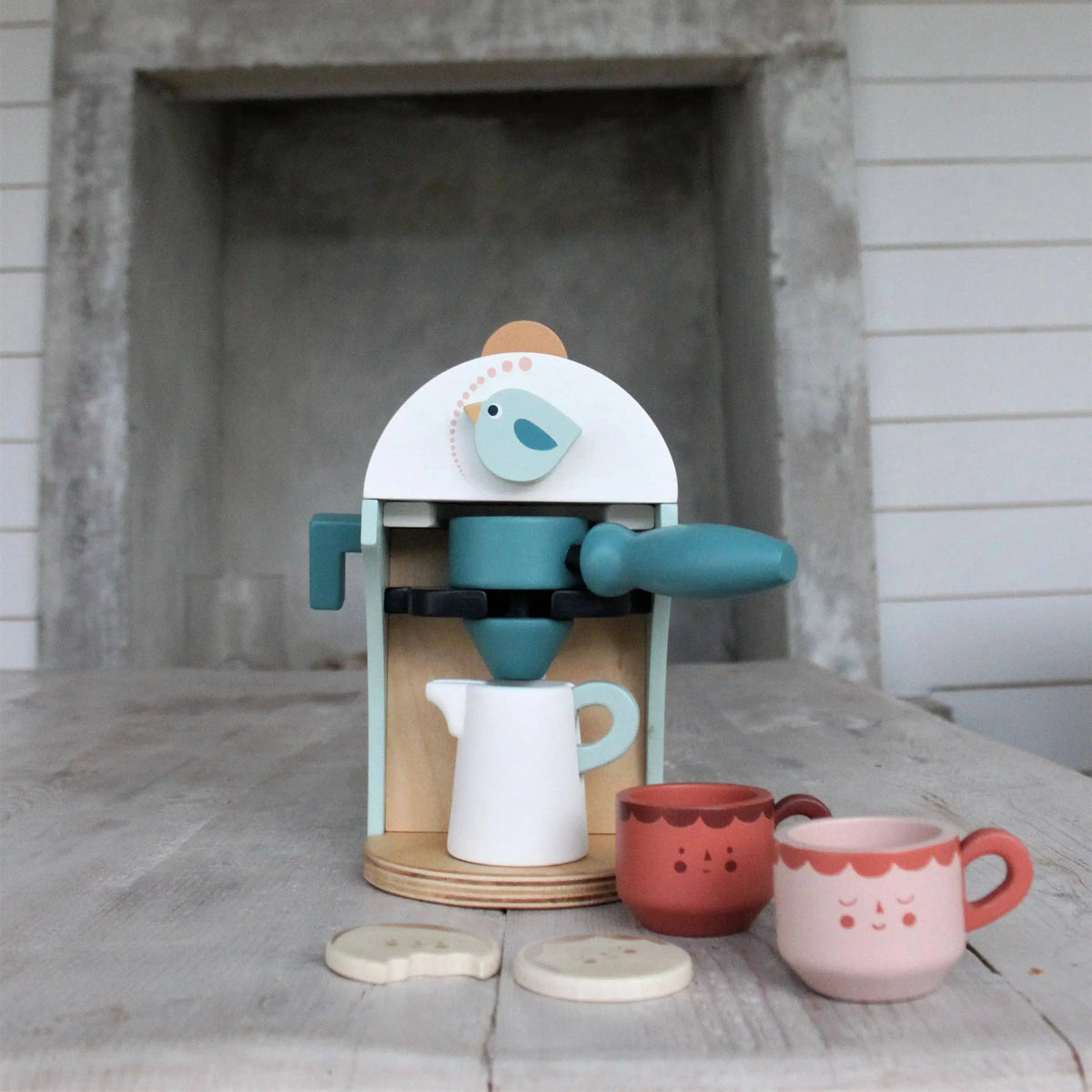 Babyccino Kaffeemaschine aus Holz mit Tassen und Zubehör in einer natürlichen Spielumgebung.