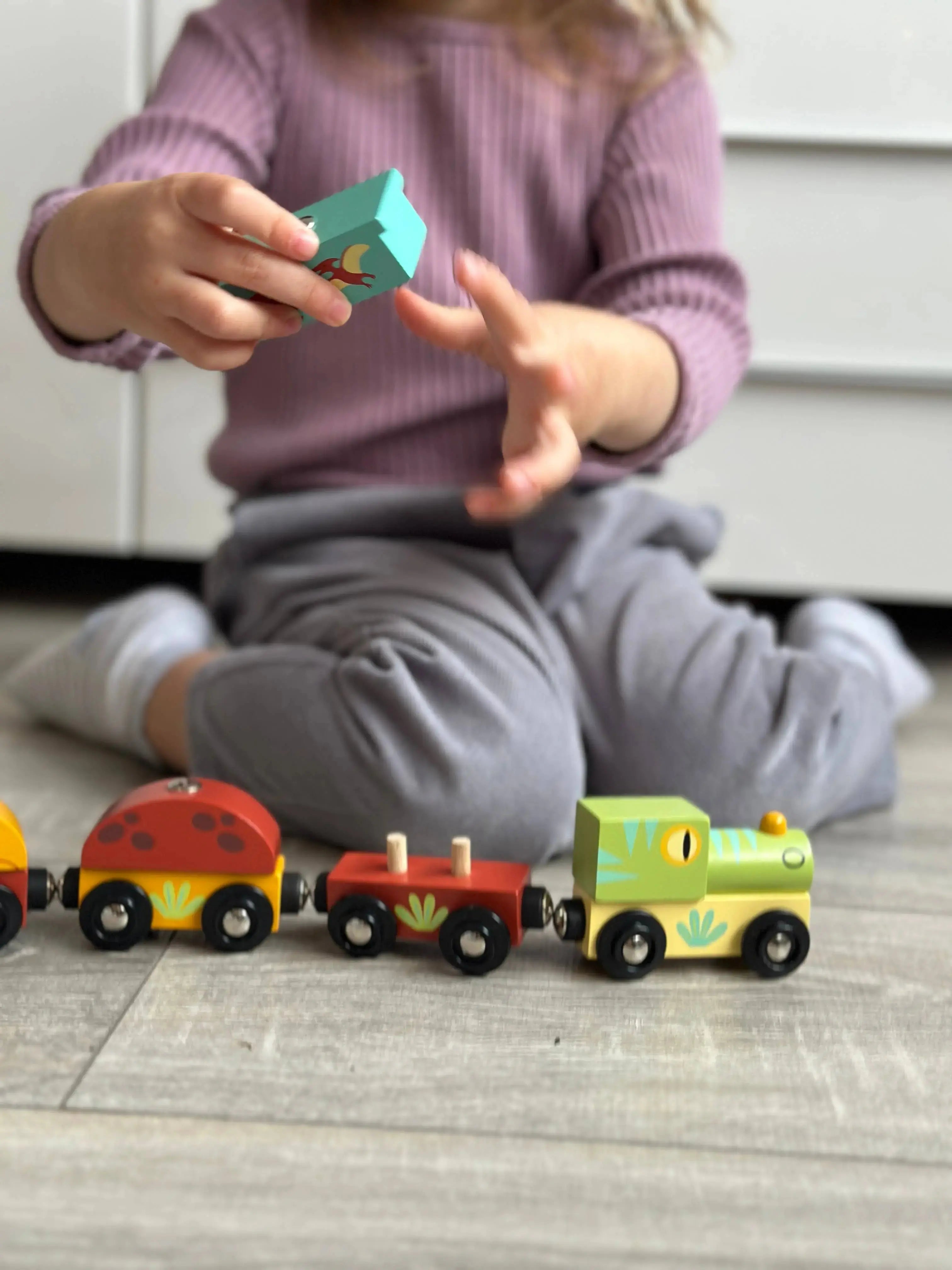 Kleinkind verbindet und bewegt die Wagen des Holz Dinosaurierzugs