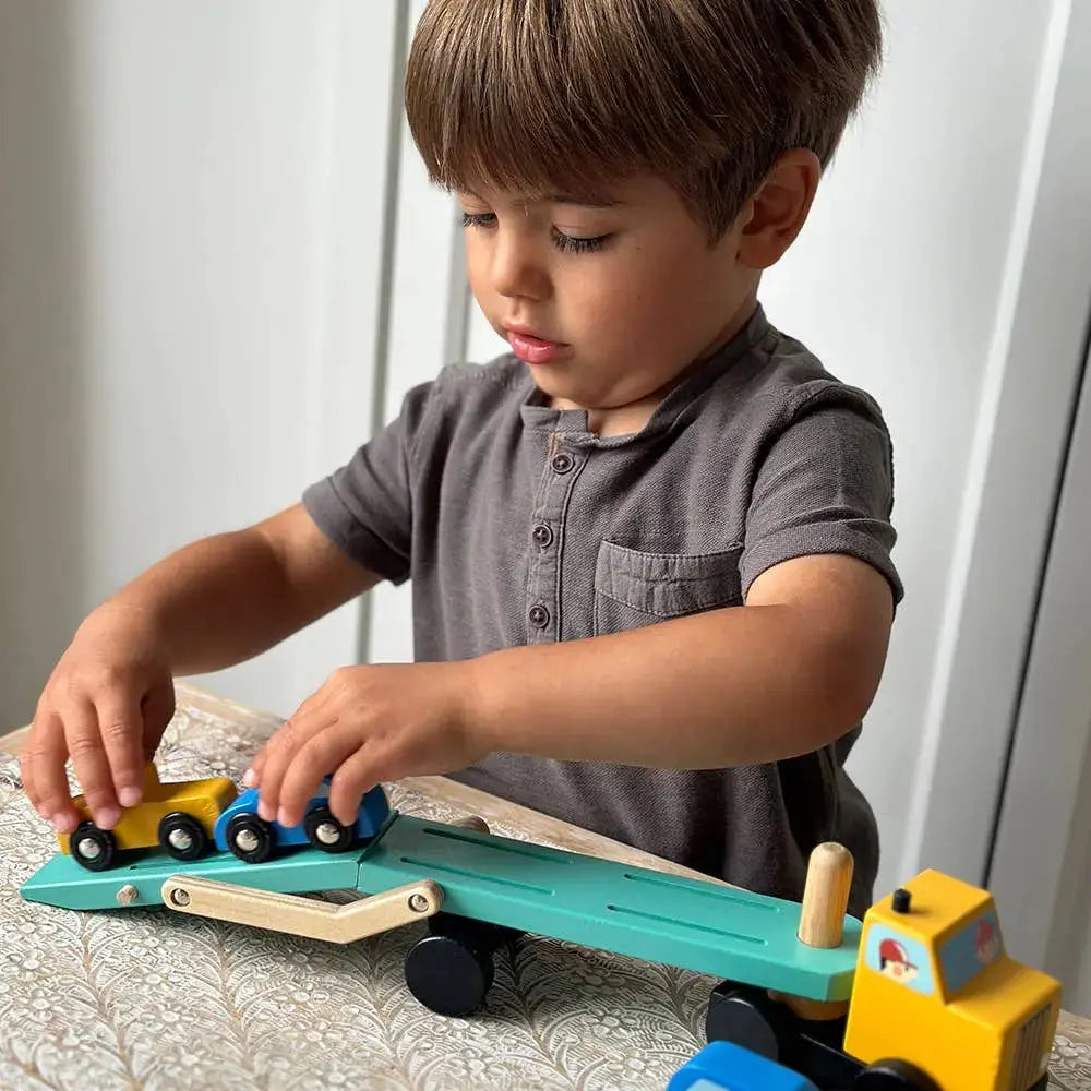 Junge beim fantasievollen Fahrzeugspiel mit dem Autotransporter aus Holz.