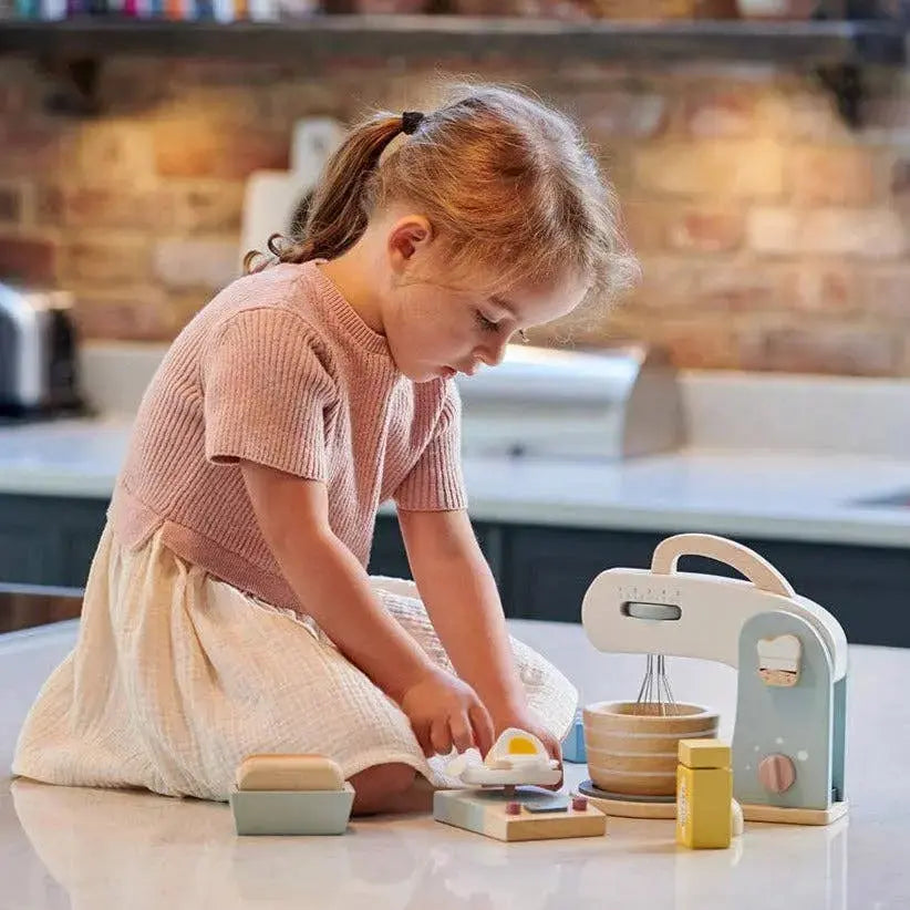 Kind beim fantasievollen Backen mit Küchenmaschine, Zutaten und Zubehör aus Holz.