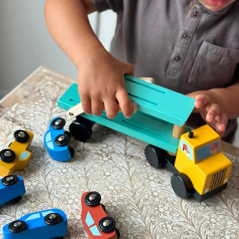 Kinderhände laden ein kleines Holzauto auf den Autotransporter.