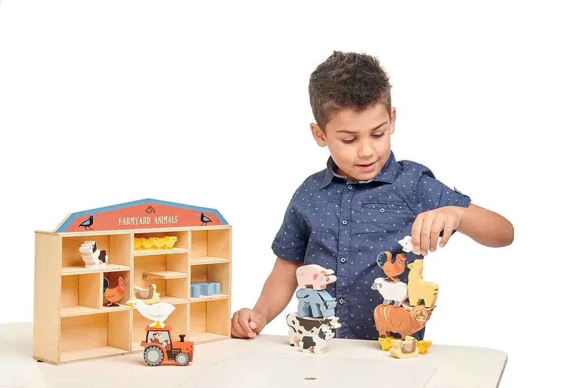 Kind spielt mit einem Bauernhof und verschiedenen Bauernhoftieren aus Holz.