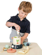 Kind bereitet beim Rollenspiel eine Suppe mit Kochtopf, Handmixer und Gemüse aus Holz zu.